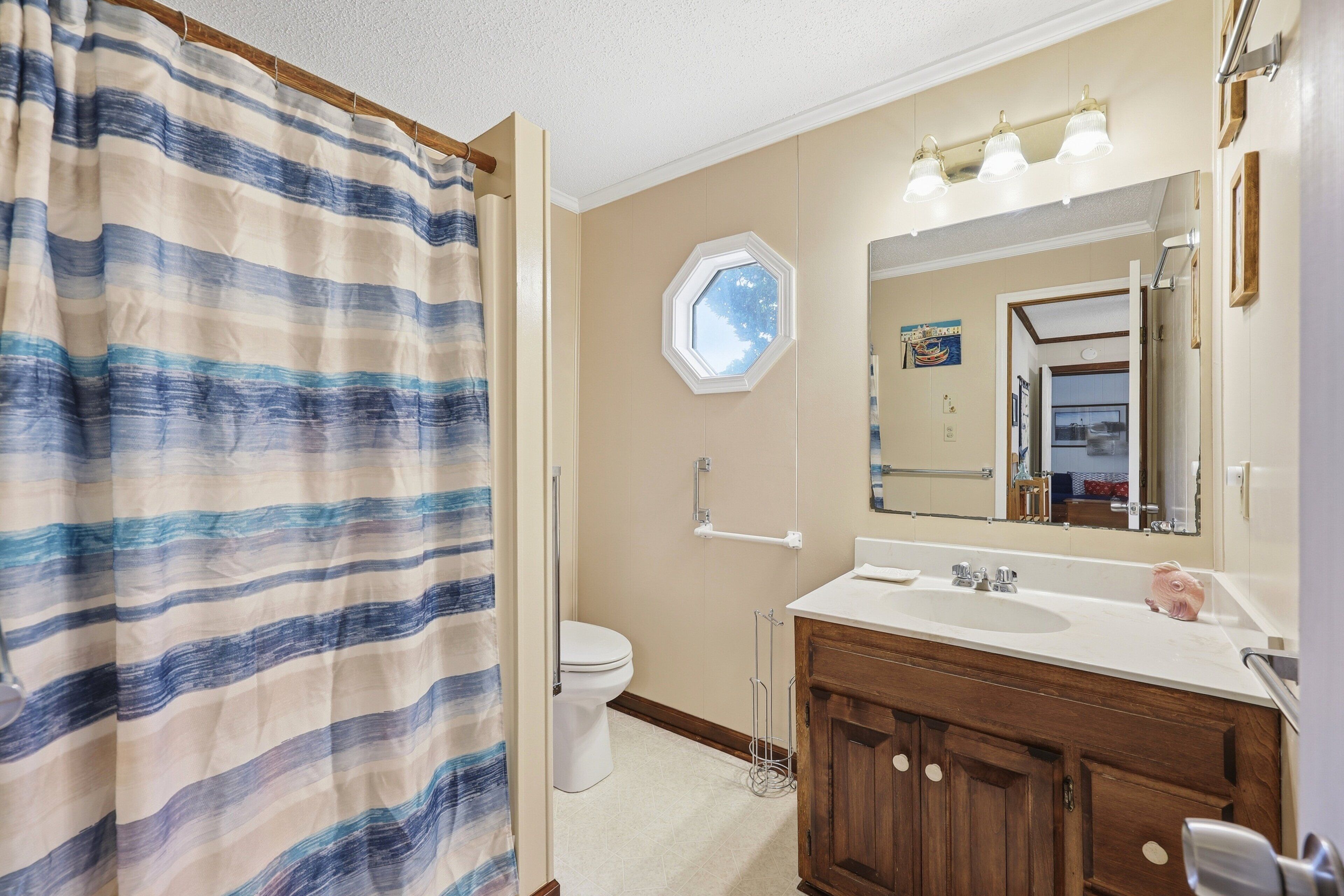A bathroom with a shower curtain, a toilet, a sink with a mirror, and a window.