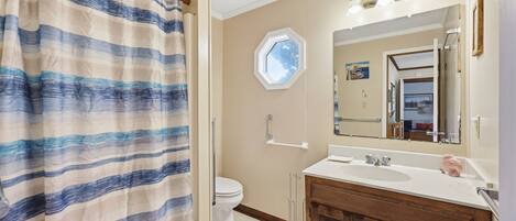 A bathroom with a shower curtain, a toilet, a sink with a mirror, and a window.