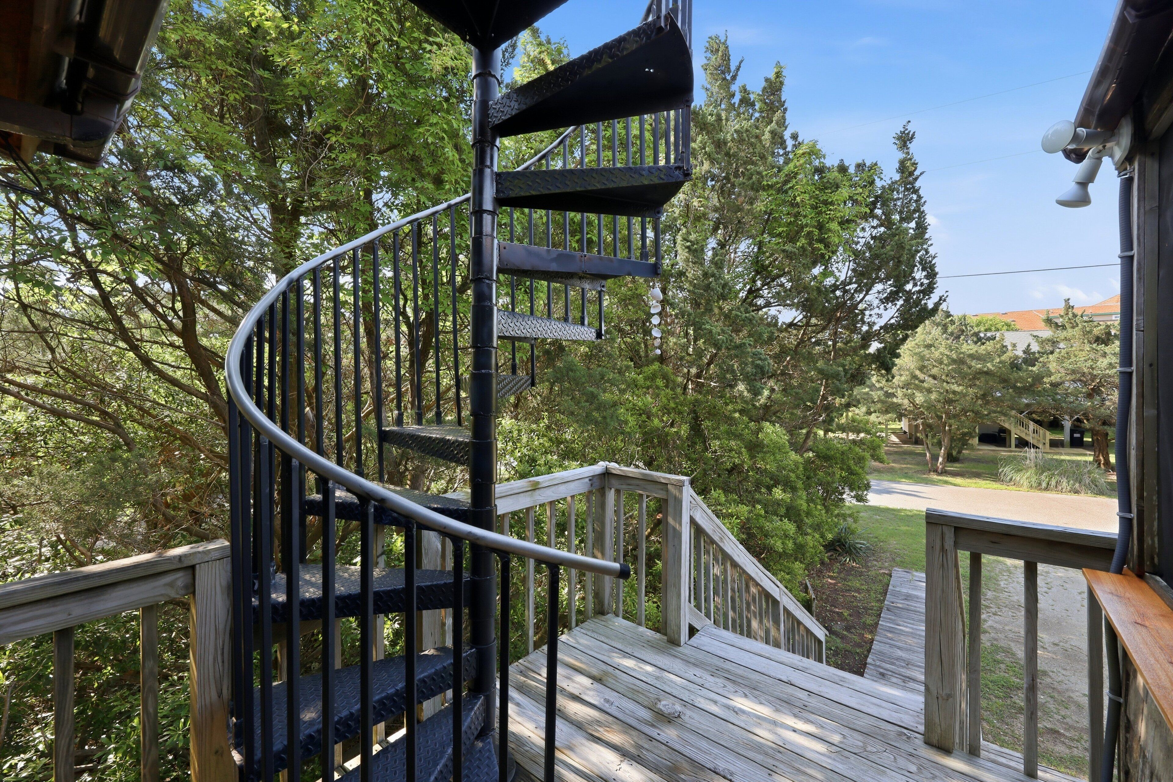 A spiral staircase leading to a wooden deck surrounded by trees.