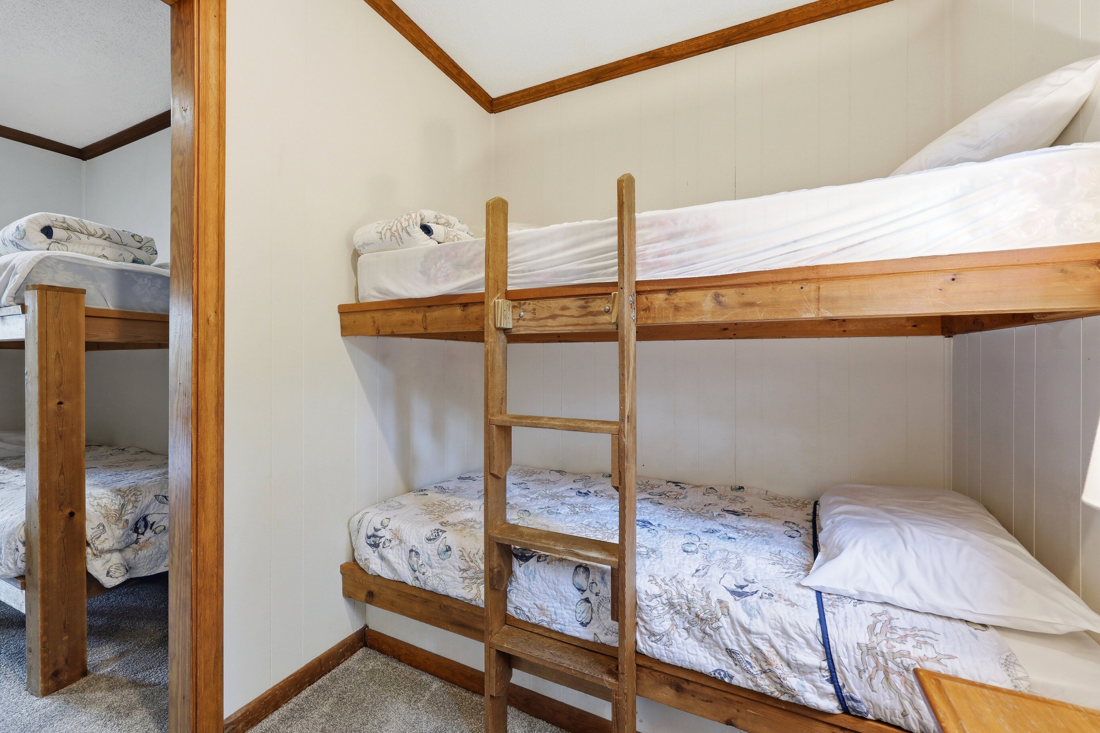 A bunk bed room with a wooden ladder, white walls, and patterned bedding.