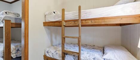 A bunk bed room with a wooden ladder, white walls, and patterned bedding.