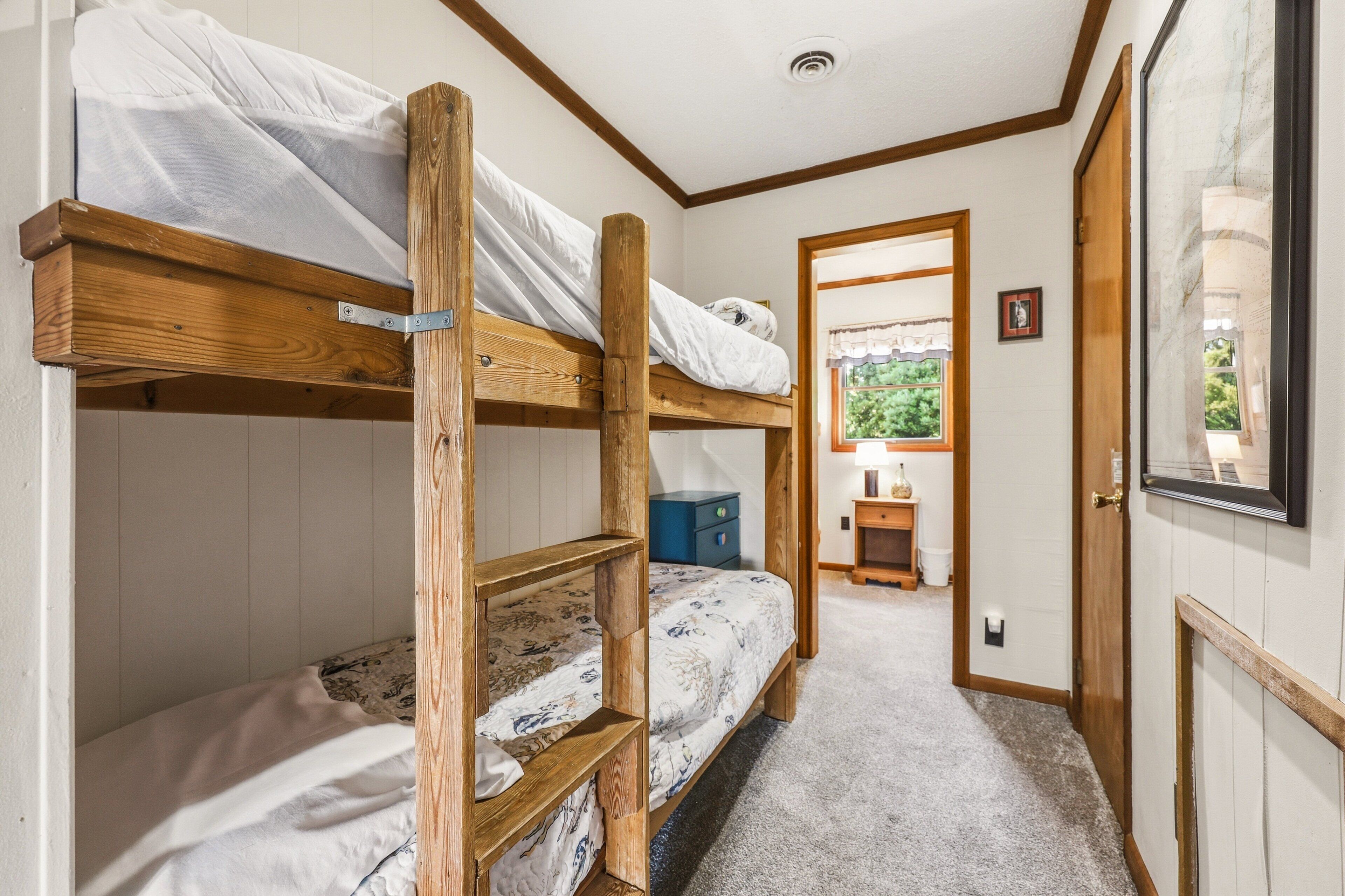 A bunk bed room with a wooden frame, a small desk, and a door leading to another room.