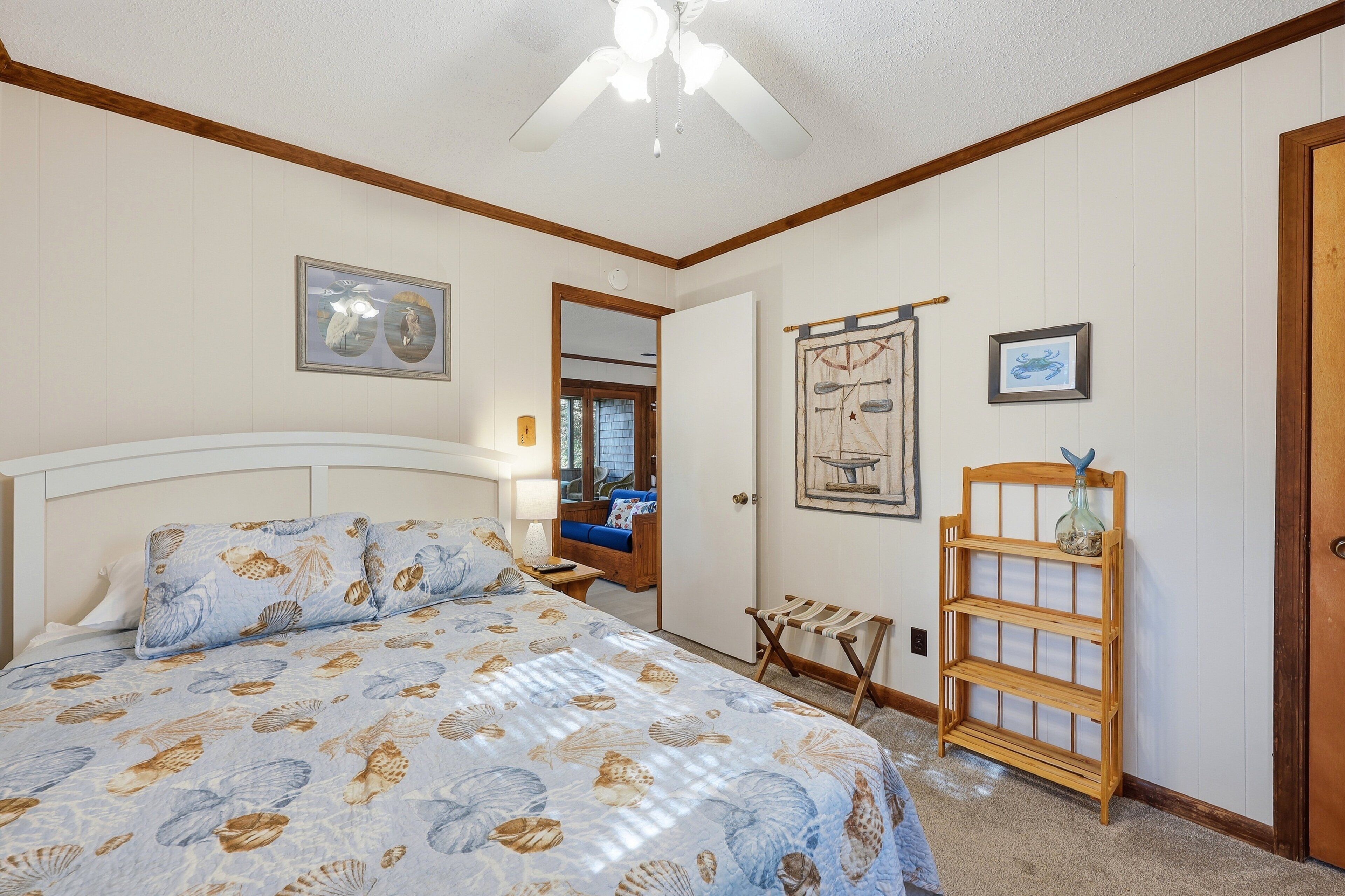 A bedroom with a bed, a wooden bench, a wall-mounted shelf, and a ceiling fan.