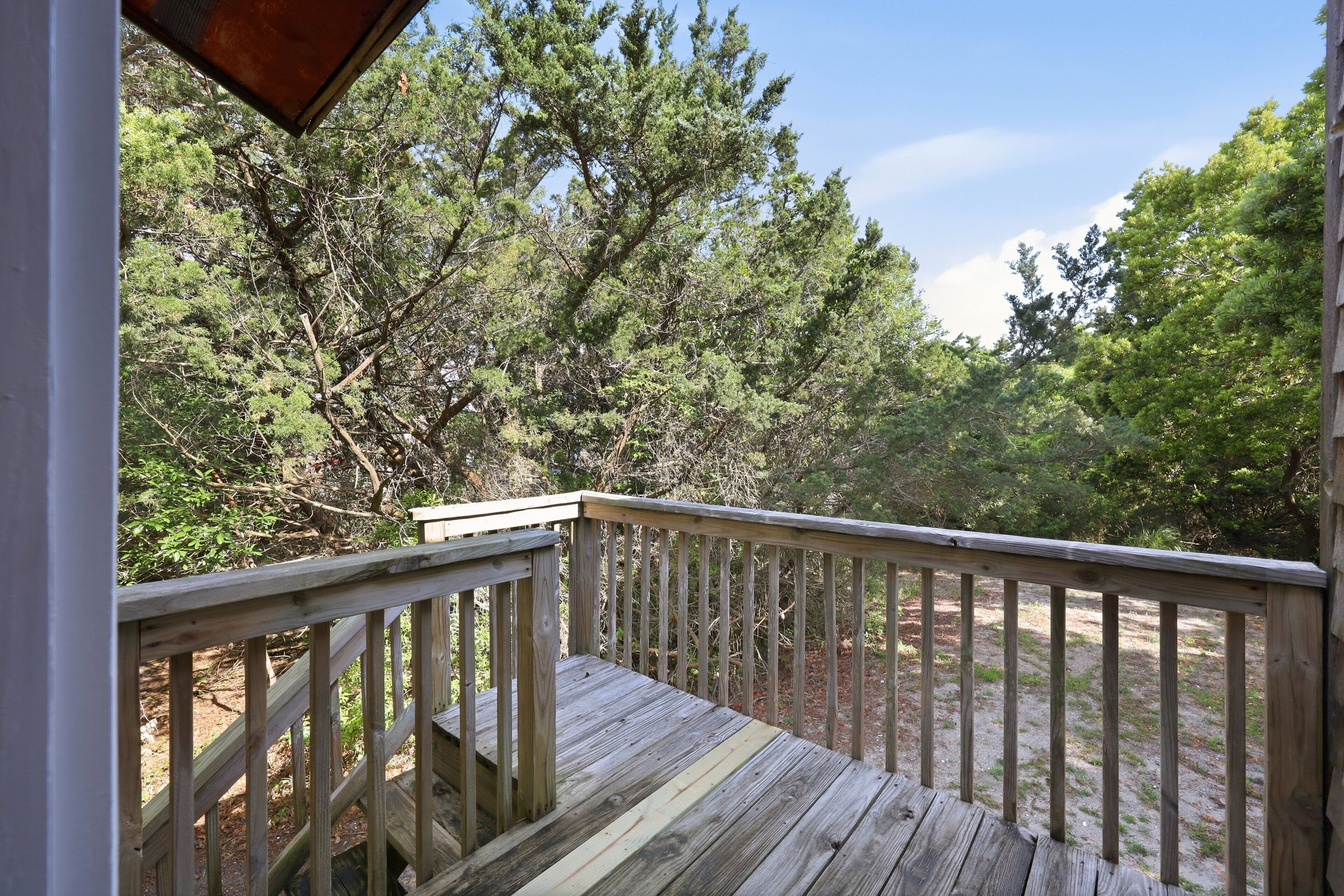 Une terrasse en bois dotée d’une rambarde, entourée d’arbres denses.