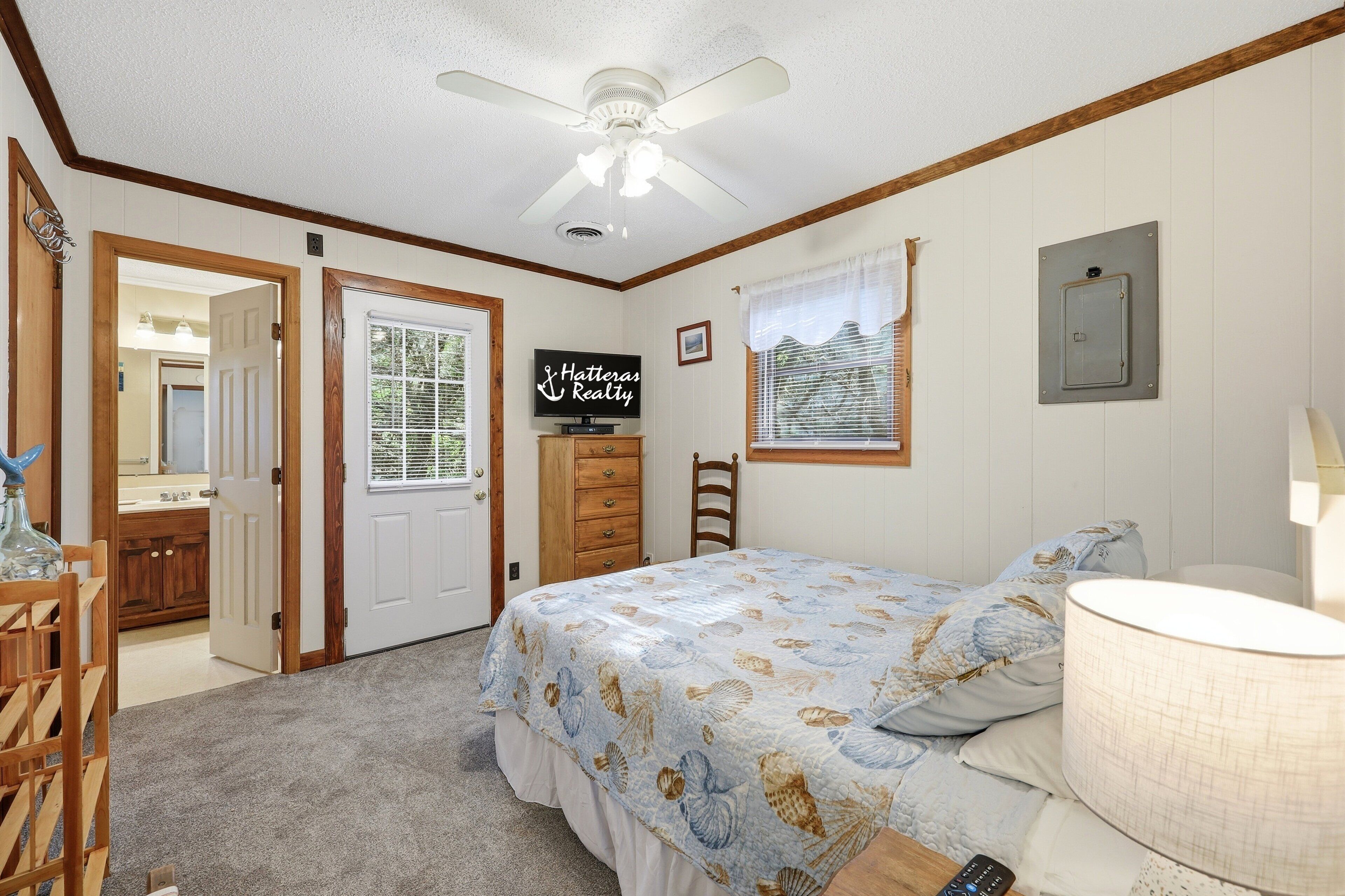 Une chambre à coucher comprenant un lit, un ventilateur de plafond, une commode, un bureau et une fenêtre avec des stores.