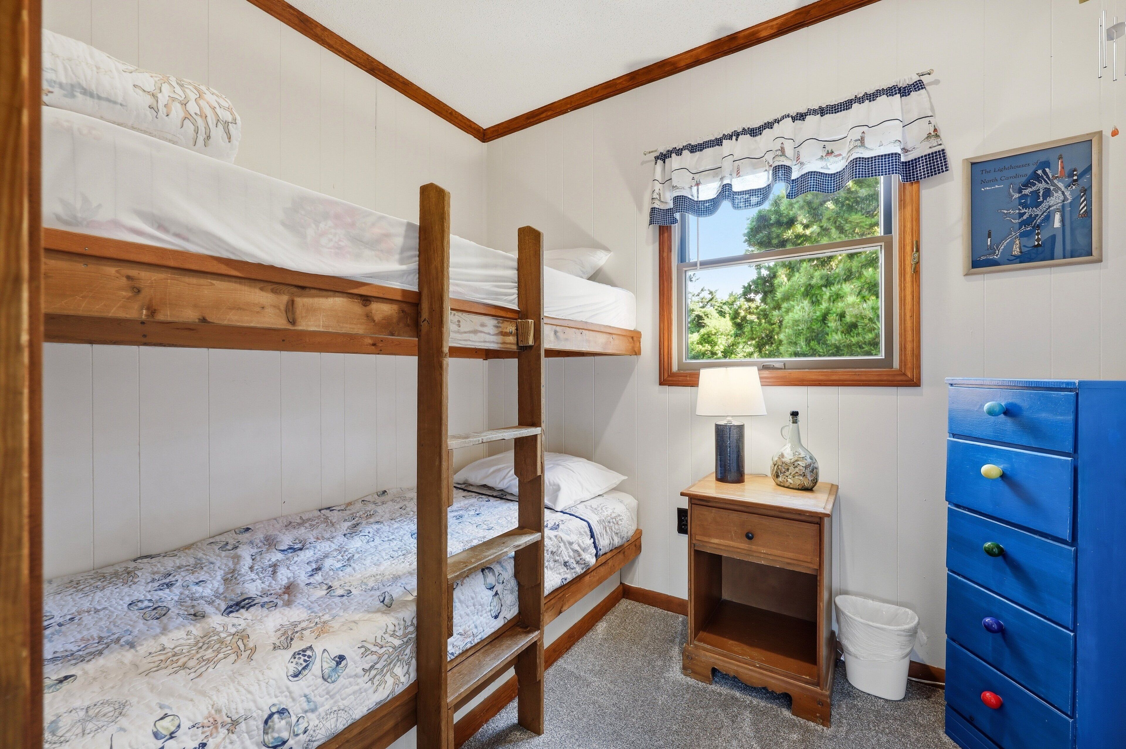 A bunk bed room with a window, a lamp, a dresser, and a framed picture on the wall.