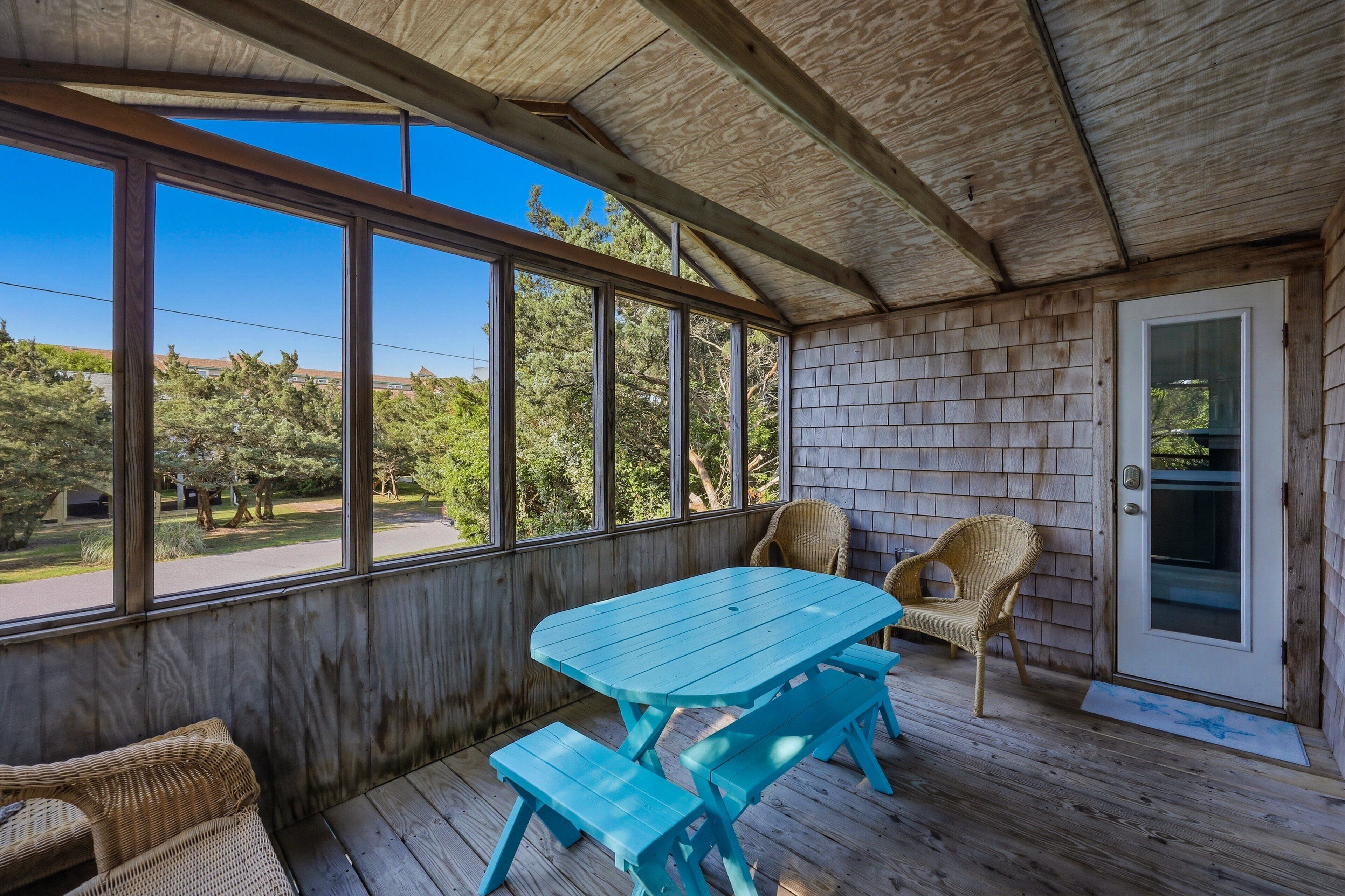 Une véranda avec une table et des bancs en bois, des chaises en osier et une porte.