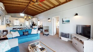 A spacious living room with a blue sofa, a glass coffee table, and a television.
