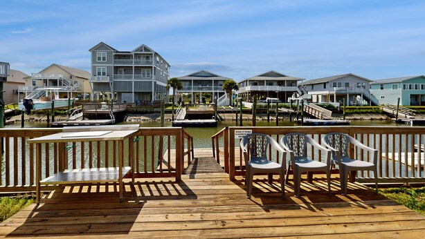 A wooden deck with chairs and a view of a marina with boats and houses.