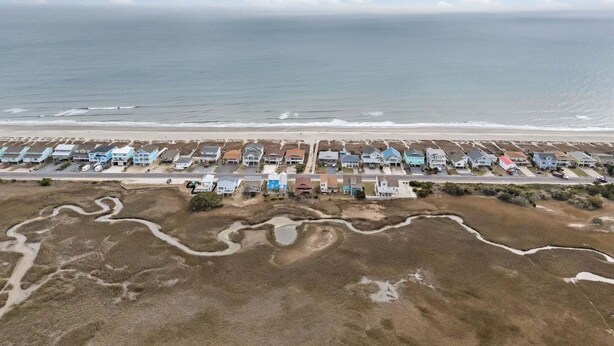 Oversigtsbillede af et kystnære boligområde med huse langs stranden, en vej og et mindre vandareal.
