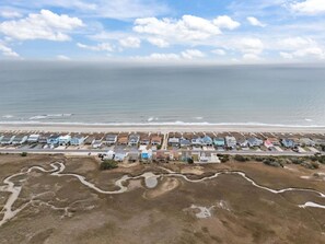 Vue aérienne d’une zone résidentielle côtière, avec des maisons alignées le long du bord de mer, une route et un petit plan d’eau.