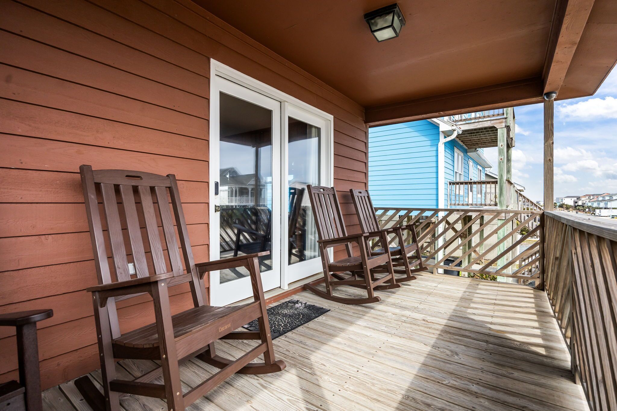 A wooden deck with rocking chairs, a door, and a view of a blue building.
