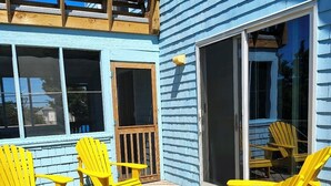 Un edificio blu con un patio in legno, poltrone Adirondack gialle e una porta scorrevole in vetro.