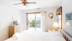 Una camera da letto con un letto, una scrivania con un computer, una finestra con tende, una ventola a soffitto e una lampada a parete.