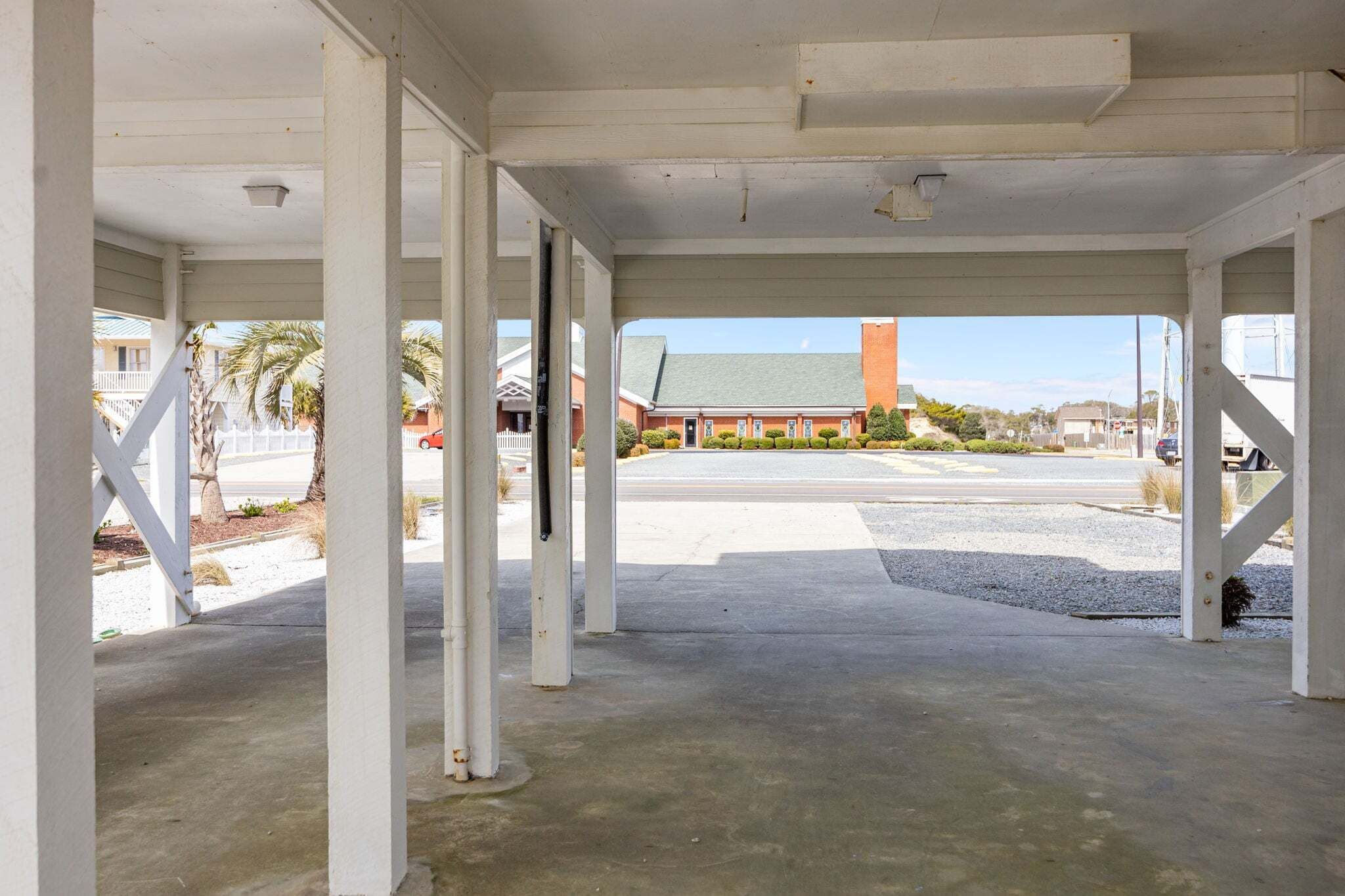 Un espace extérieur abrité, doté d’un sol en béton et de colonnes blanches en béton apparent.