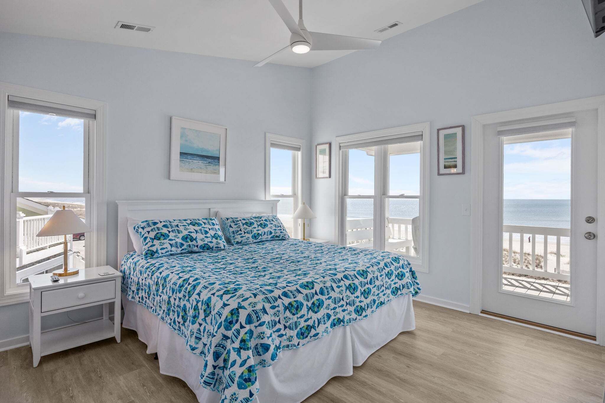 Un dormitorio con cama, mesita de noche, lámpara y vista a la playa.