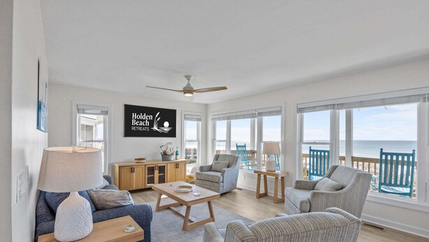 Amplia sala de estar con vista a la playa, un ventilador de techo y un cartel que dice 'Golden Beach Retreats'.