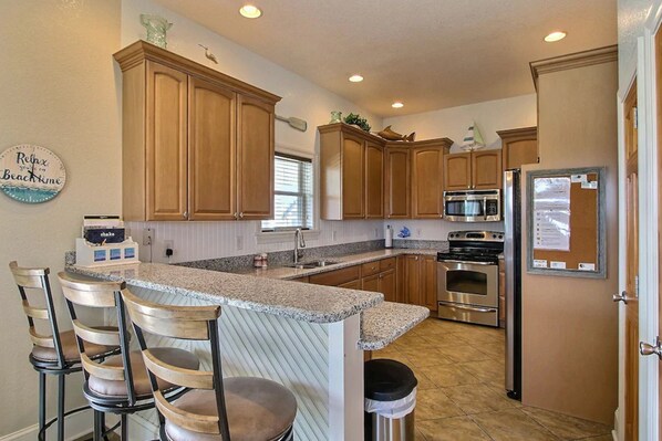 A kitchen with wooden cabinets, granite countertops, a stainless steel refrigerator, and a built-in oven. - Dog-friendly home with private pool, hot tub, ocean view, & high-speed WiFi (Buxton)