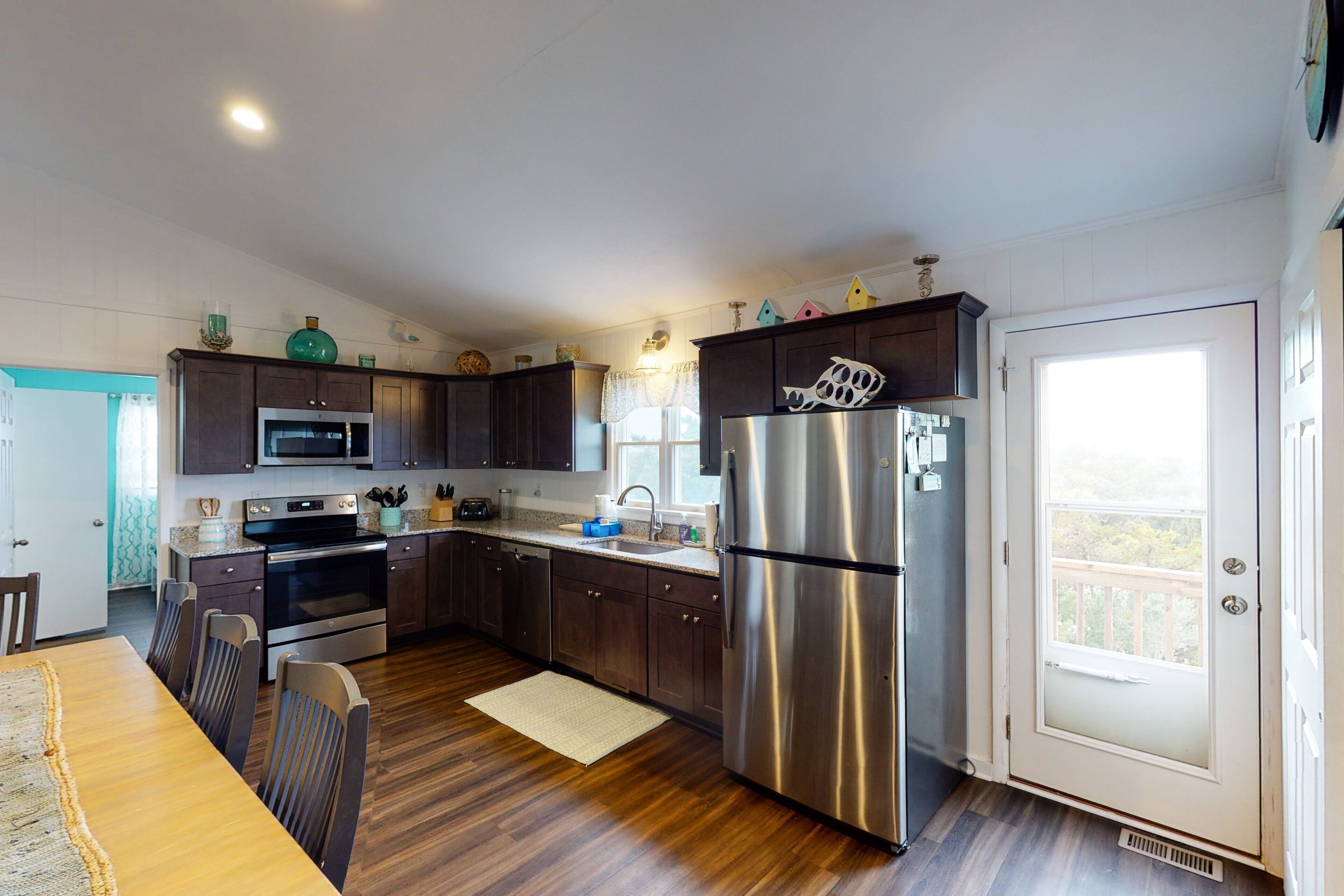 Une cuisine moderne avec des meubles en bois foncé, des appareils électroménagers en acier inoxydable et un coin repas comprenant des chaises et une table en bois.