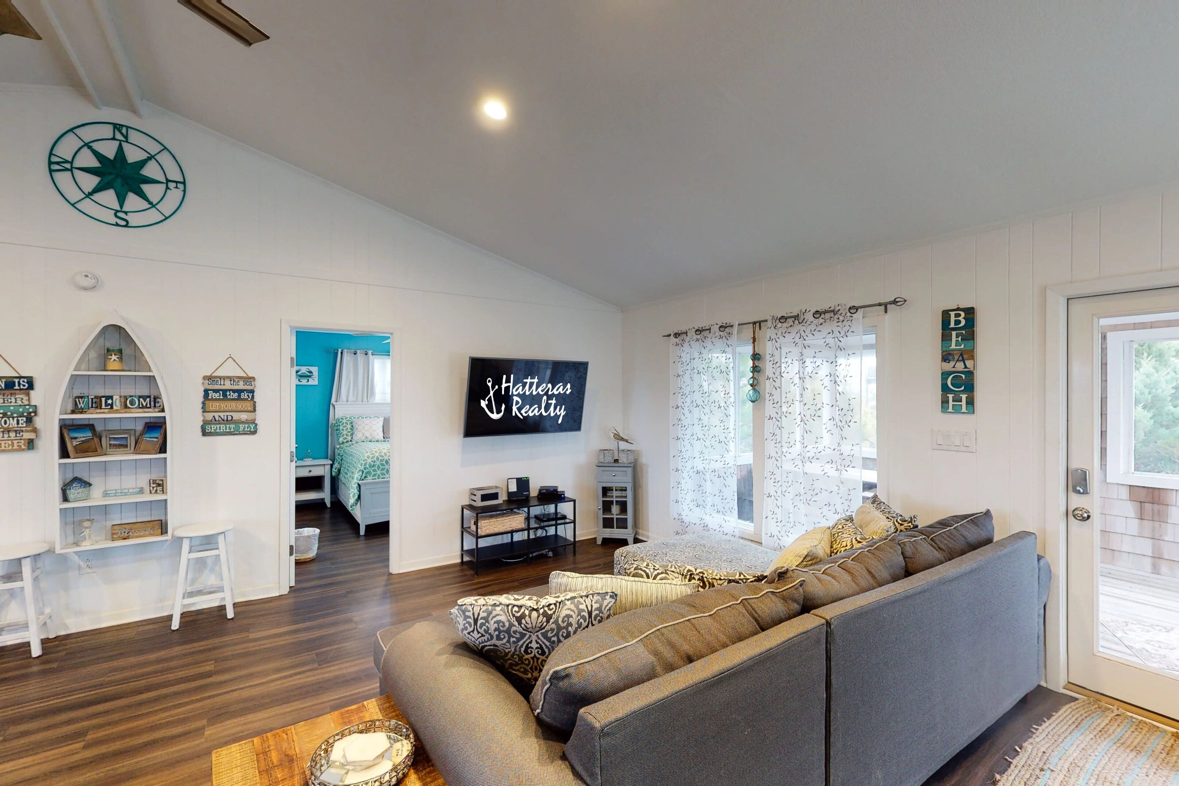 A modern living room with a grey sectional sofa, a flat-screen TV, and a wall-mounted compass.