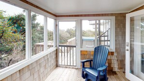 A corner room with a wooden deck, a blue chair, and large windows offering a view of the outdoors. - Twin Tides #14-AC: Semi-Oceanfront, Dog-Friendly, Shared Pool, Hot Tub (Avon)