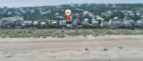 An aerial view of a coastal residential area with houses, a beach, and ocean waves.