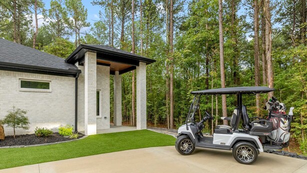 A modern house with a covered porch, a well-maintained lawn, and a golf cart parked in front.
