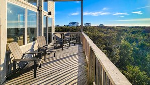 A wooden deck with Adirondack chairs and a view of a forested landscape. - Carolina Breeze 488: Nature lover's home, sound-front with great views, shared pool (Avon)