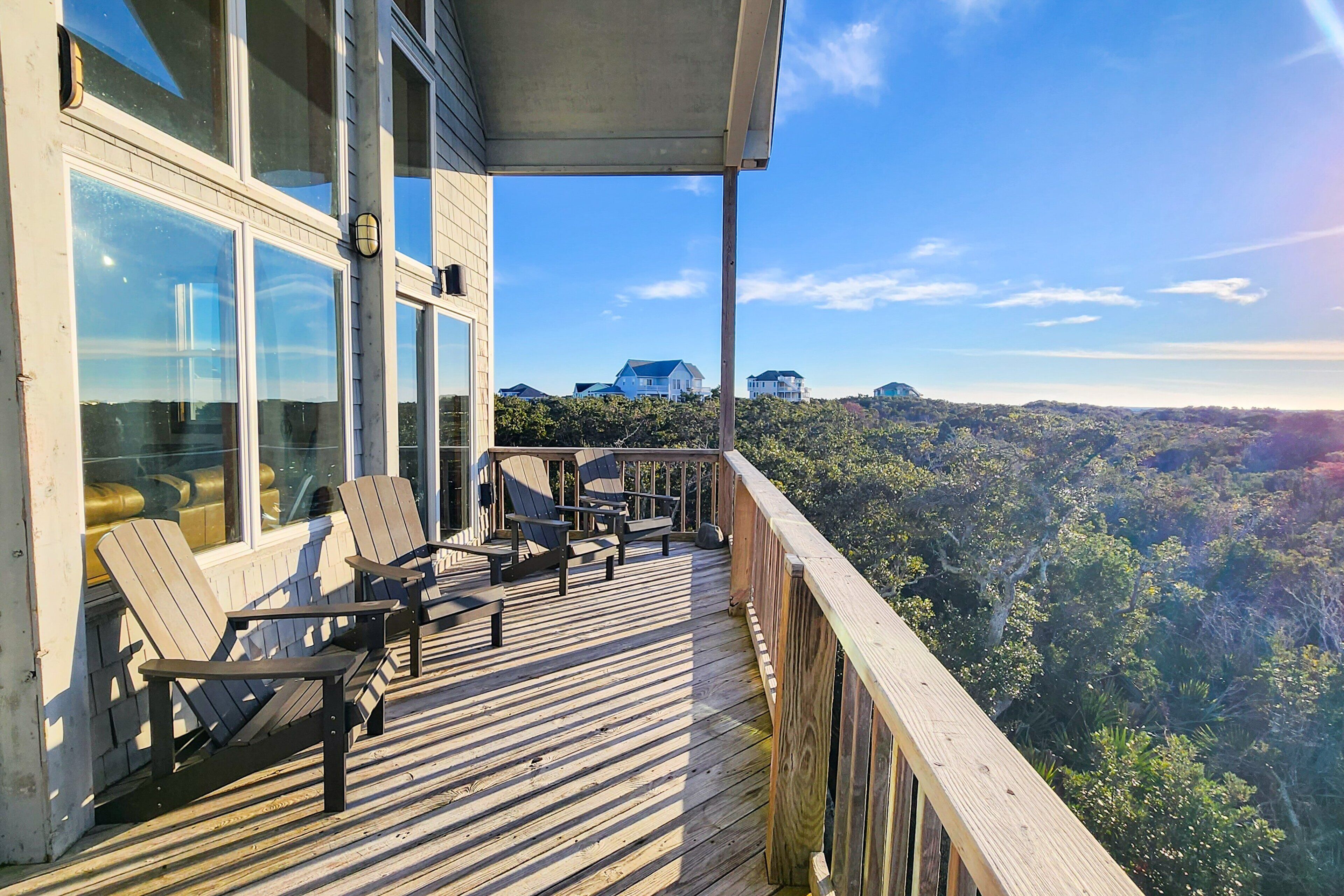 Una terraza de madera con sillas Adirondack y vista a un paisaje boscoso.
