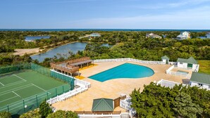 A large swimming pool surrounded by a wooden deck and tennis courts, with a view of the ocean and surrounding greenery. - Carolina Breeze 488: Nature lover's home, sound-front with great views, shared pool (Avon)