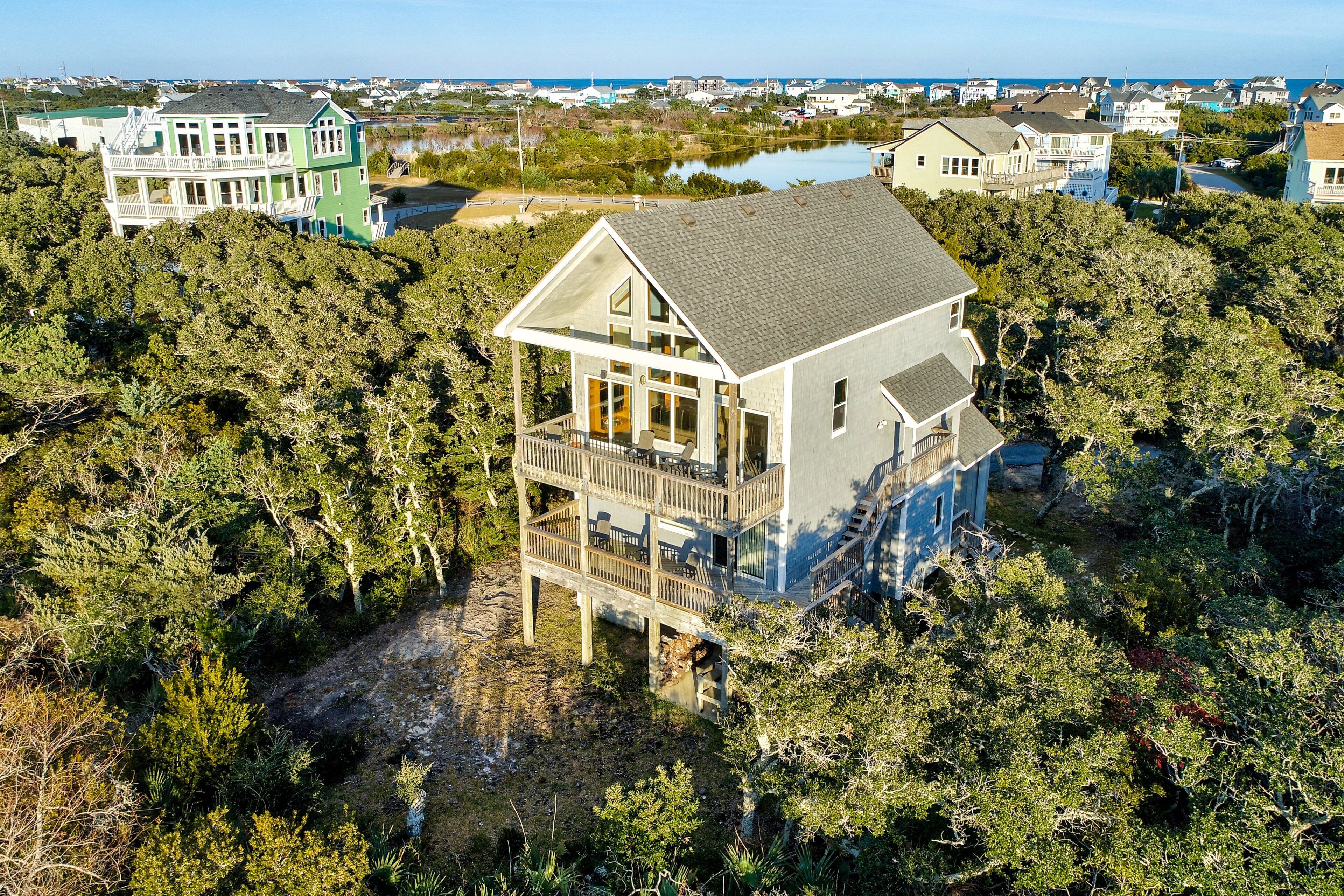 A two-story house with a balcony, surrounded by dense trees and a lake in the background.
