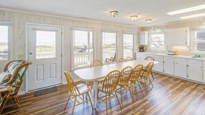 A spacious dining area with a long table and several chairs, large windows, and a view of the outside. - Shiloh by the Sea: Ocean-View Home with Easy Beach Access, WiFi & Central AC (Holden Beach)