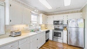 A modern kitchen with white cabinets, stainless steel appliances, and a wooden floor. - Shiloh by the Sea: Ocean-View Home with Easy Beach Access, WiFi & Central AC (Holden Beach)