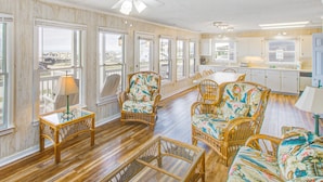 A spacious living area with wicker furniture, a glass coffee table, and a ceiling fan. - Shiloh by the Sea: Ocean-View Home with Easy Beach Access, WiFi & Central AC (Holden Beach)