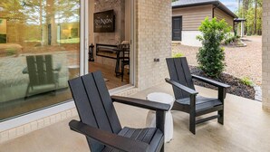 A modern outdoor seating area with two Adirondack chairs, a glass door leading to a dining area, and a sign for 'The Reunion Resort Villas'. - Reunion Resort Studio Unit 113A (Hot Springs Village)