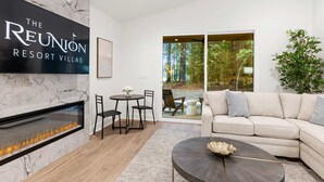 A modern living room with a fireplace, a sofa, a coffee table, and a dining area with chairs. - Reunion Resort Studio Unit 113A (Hot Springs Village)