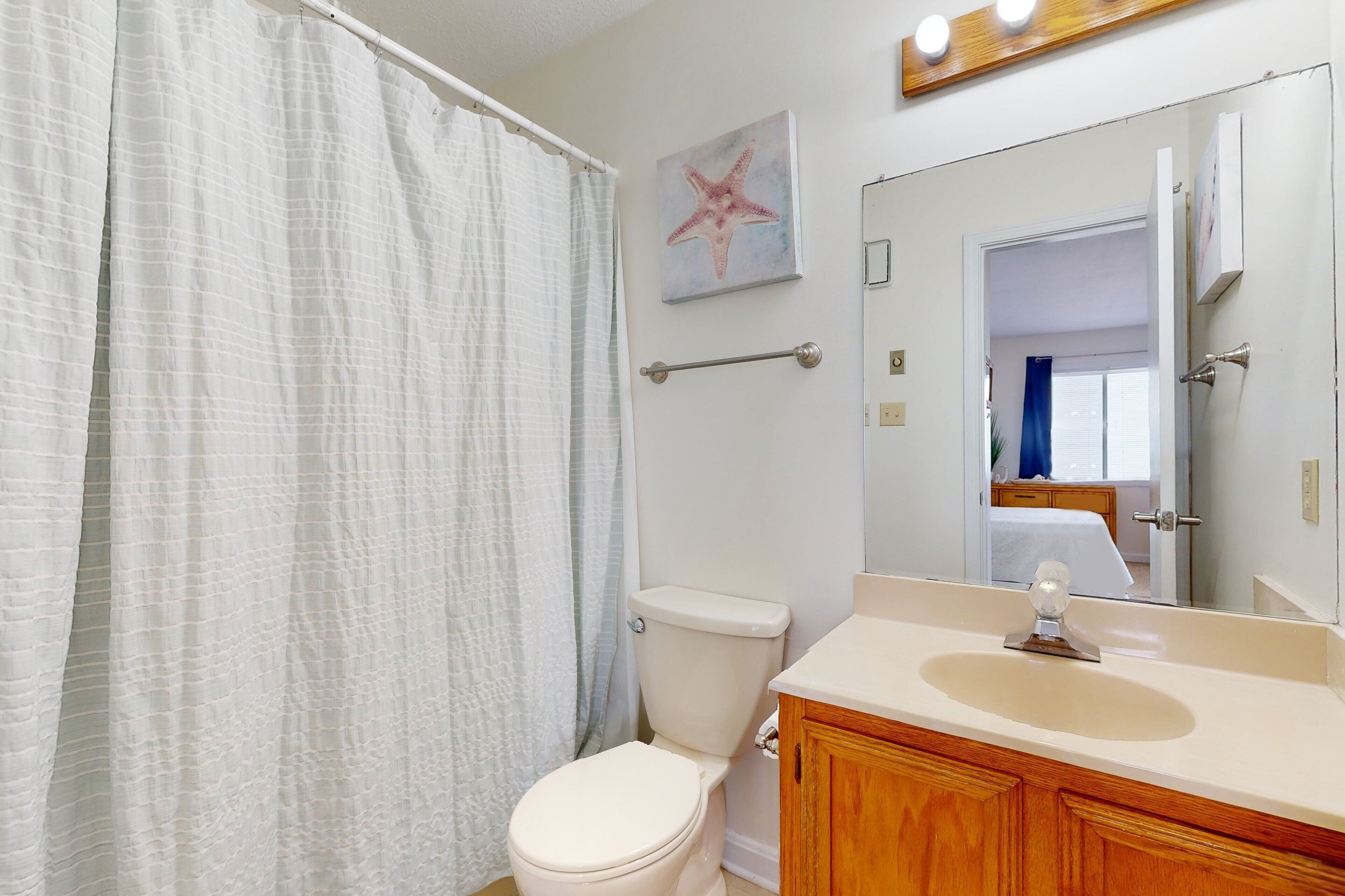 A bathroom with a toilet, a sink, a mirror, and a shower curtain.