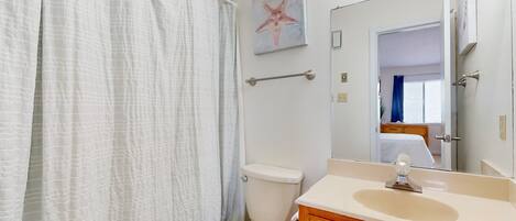 A bathroom with a toilet, a sink, a mirror, and a shower curtain.