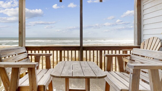 Une terrasse en bois avec une table et des chaises donnant sur une plage.