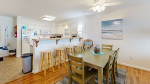 Une cuisine moderne avec des meubles blancs, un îlot central doté de tabourets et un coin repas avec des chaises en bois.