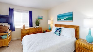 Une chambre à coucher avec un lit, des tables de chevet en bois, une télévision, une lampe et une fenêtre avec des rideaux.