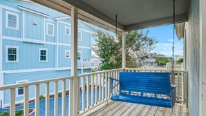 Une véranda en bois avec un banc bleu, des balustrades blanches et une vue sur un immeuble bleu doté de fenêtres et d’un balcon.