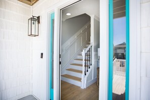 Um corredor com escada de madeira, porta com moldura azul-turquesa e luminária fixada na parede.