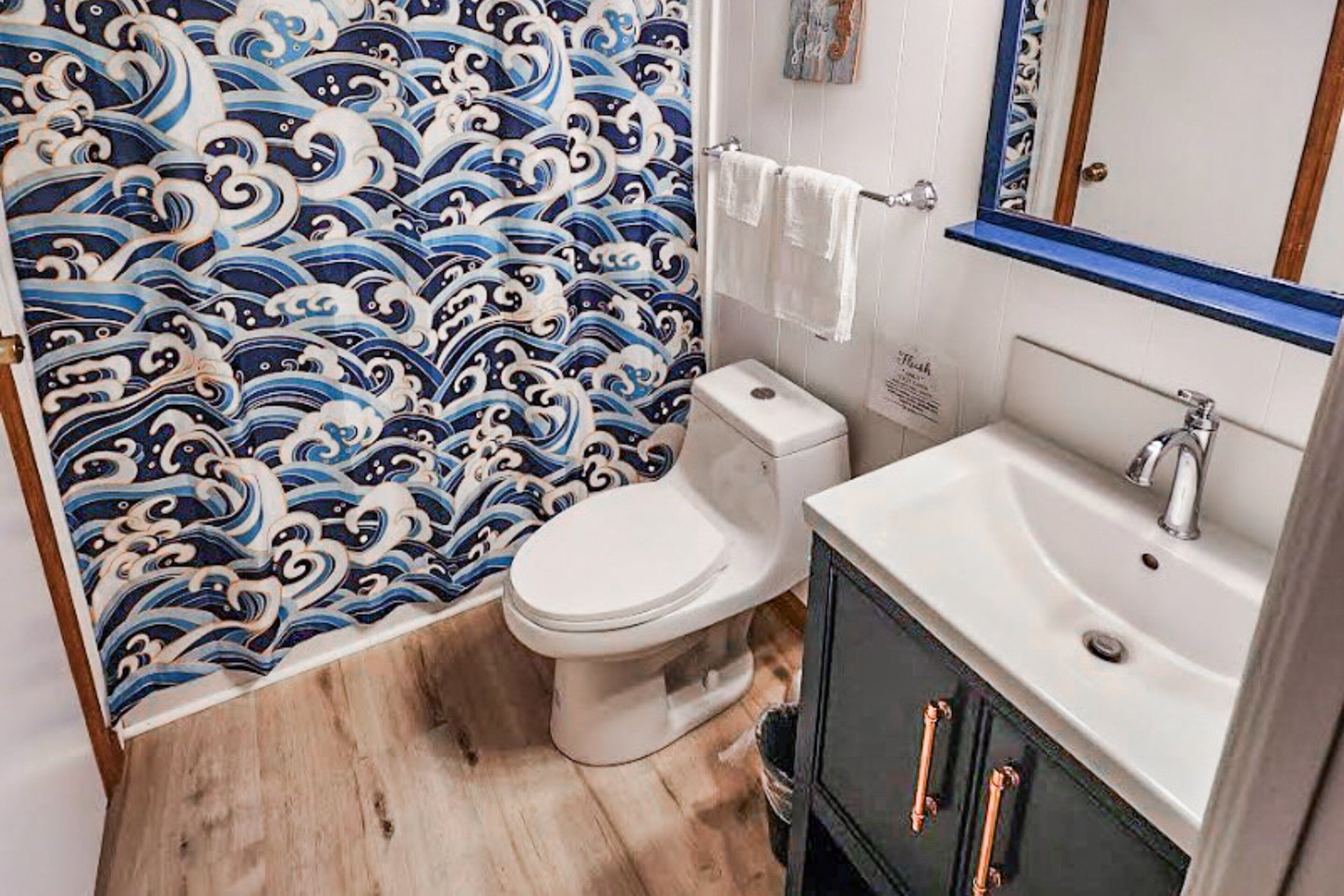A bathroom with a traditional Japanese wave pattern wallpaper, a white toilet, a sink with a mirror, and a black cabinet with copper handles.