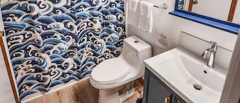 A bathroom with a traditional Japanese wave pattern wallpaper, a white toilet, a sink with a mirror, and a black cabinet with copper handles.