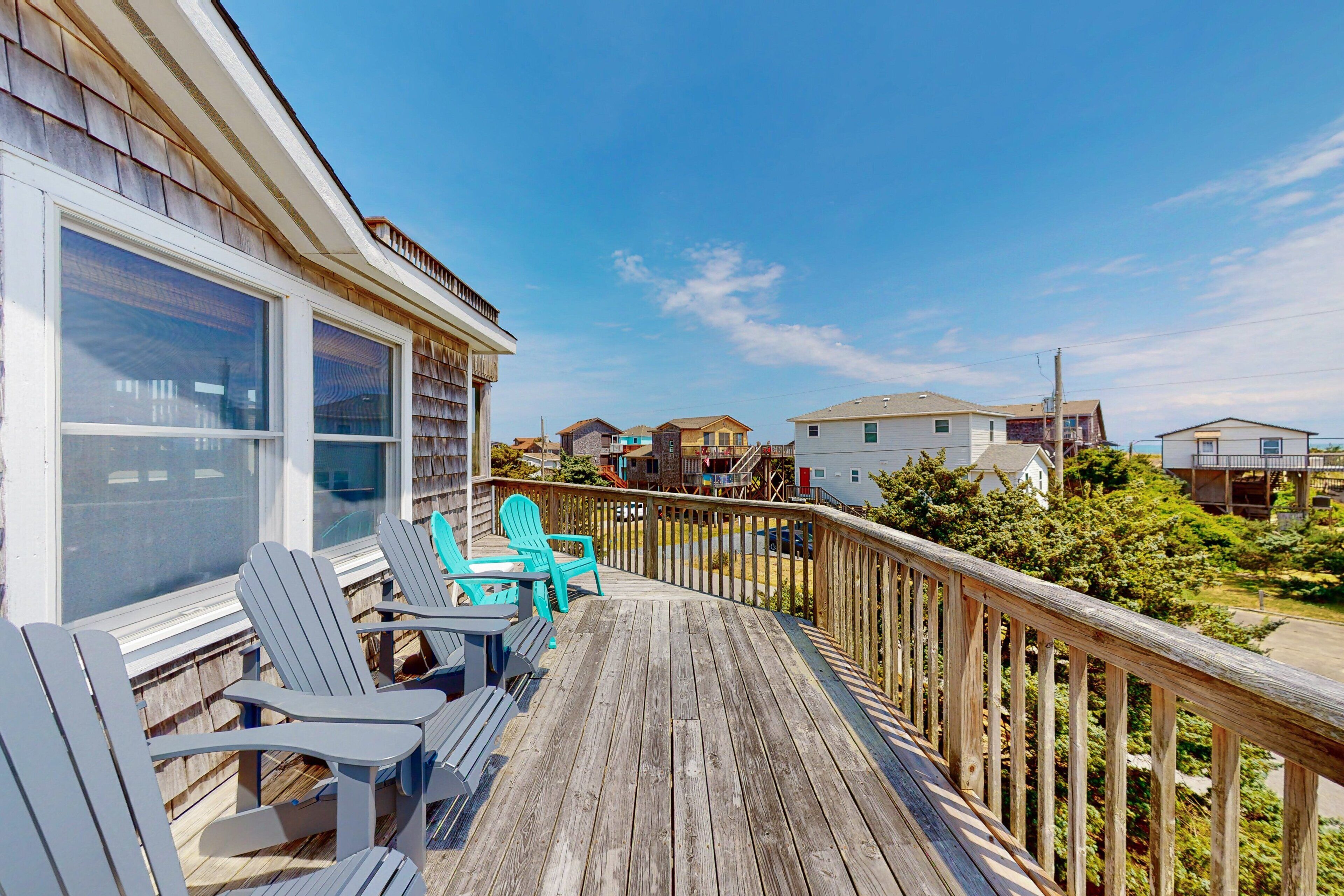 A wooden deck with Adirondack chairs, a railing, and a view of neighboring houses.