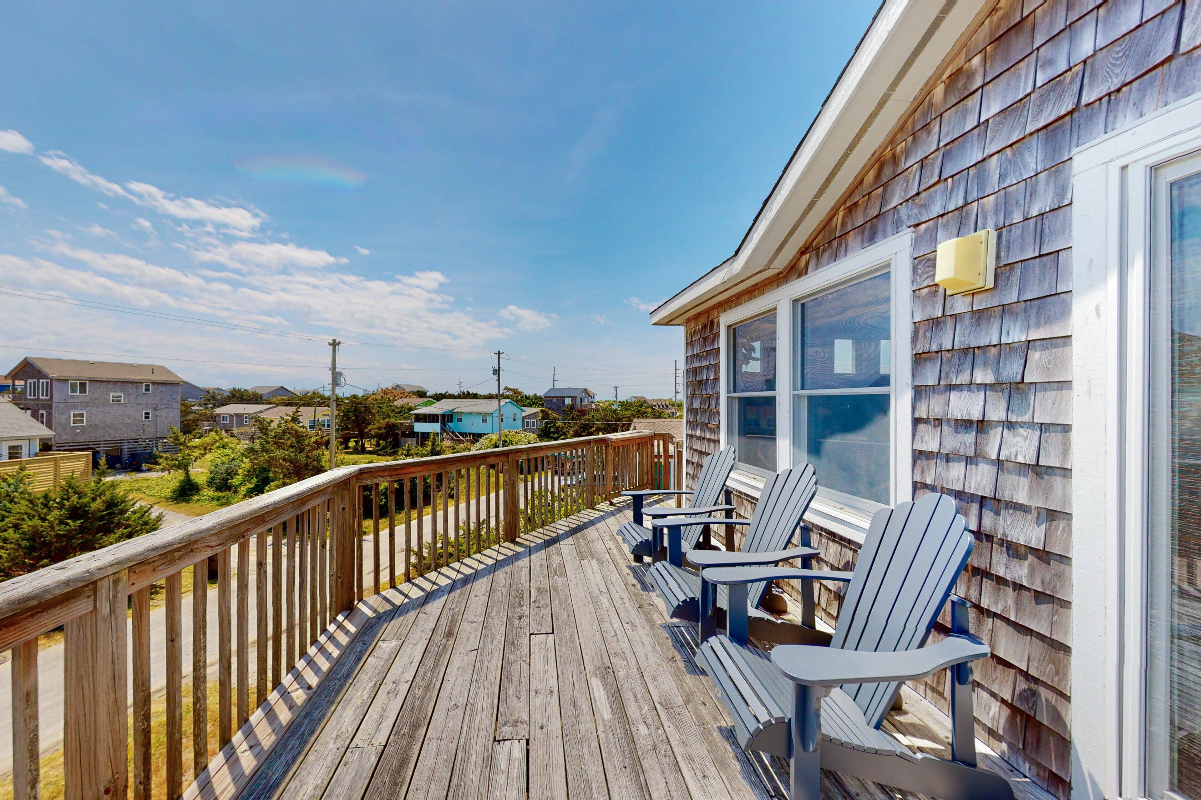 A wooden deck with Adirondack chairs, a railing, and a view of neighboring houses.