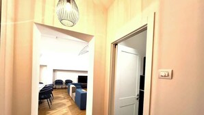 A hallway leading to a dining area with a table and chairs, a sofa, and a television.
