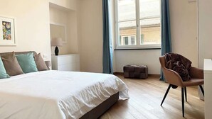 A modern bedroom with a large bed, a chair, a desk, and a window with curtains.