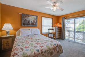 A bedroom with a bed, a ceiling fan, a window with blinds, a nightstand with a lamp, and a dresser with drawers. - Canal-Front Home & Porch - Floating Boat Dock, Central AC, Outdoor Shower, WiFi (Holden Beach)
